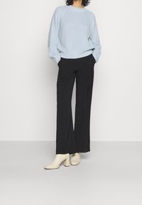 Ljusblå stickad tröja med rund halsringning, i kombination med svarta vida byxor och krämfärgade klackade ankelskor.