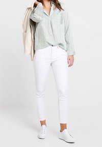 Hellgrünes gestreiftes Hemd, weiße Skinny-Jeans und weiße Sneakers. Das Hemd hat einen Kragen, eine Brusttasche und lange Ärmel.