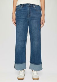 Brede blauwe denim jeans met een opgezoomde zoom en een lichte vervaging, met vijf zakken en een knoopsluiting bij de taille. Gecombineerd met witte sneakers.