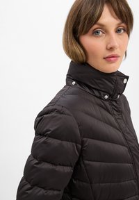 Black quilted puffer jacket with a high collar, snap buttons, and a smooth, shiny texture. Focus on contoured, padded design.