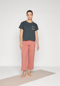 Cotton short-sleeve t-shirt in dark teal with a circular graphic, paired with soft, cropped, rose-colored pants. Simple design, relaxed fit.