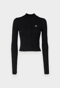 Suéter negro cropped con cremallera, presenta una textura acanalada, un cuello alto y un pequeño detalle de logo en el lado izquierdo del pecho, con mangas largas y ajustadas.