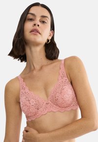 Ροζ δαντελένιο σουτιέν με κυματιστά άκρα, λουλουδένιο μοτίβο και ρυθμιζόμενους ιμάντες. Διαθέτει κούμπωμα με αγκράφα στην πλάτη και απαλή υφή.