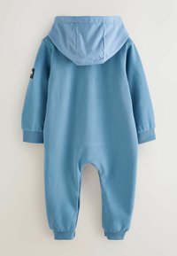 Tuta intera blu realizzata in materiale morbido, con cappuccio, polsini elastici e aperture per le gambe. Texture liscia con un design semplice e a tinta unita.