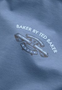 Pelēks audums ar gludu tekstūru, kurā ir drukāts logo: "BAKER BY TED BAKER" baltā un tumši brūnā krāsā, papildināts ar dekoratīviem elementiem.