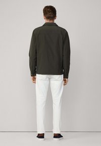 Ciemnooliwkowa kurtka z kołnierzykiem zapinanym na guziki, długimi rękawami i prostym krojem. Połączona z białymi spodniami i granatowymi trampkami.