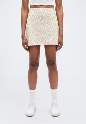 Beež miniseelik abstraktse valge mustriga, sileda tekstuuri ja istuva vöökohaosaga. Stiilitud valgete jalanõude ja sokkidega.