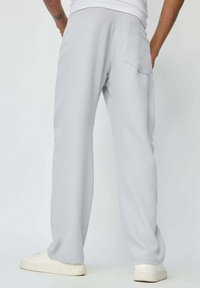 Pantalons de survêtement gris clair à coupe décontractée, dotés d'une poche arrière et d'une taille élastique, associés à des baskets blanches.