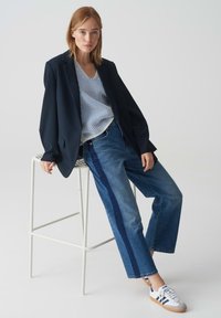 Navy blazer over blue and white striped blouse, paired with denim jeans featuring navy side stripes and white sneakers with blue accents.