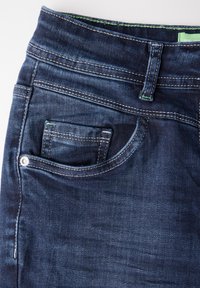 Dark blue denim jeans with a smooth texture, featuring a front pocket, contrasting white stitching, and a green accent on the waistband.