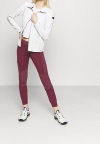 Vit zip-up fleecejacka med svarta detaljer, tillsammans med vinröda tajta byxor med färgblockering och svarta och vita sportskor.