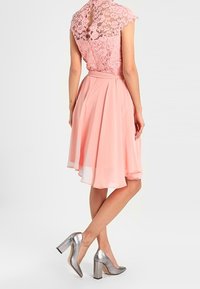 Světle růžové šaty s krajkovým korzetem, krátkými rukávy a splývavou šifónovou sukní. V kombinaci se stříbrnými botami na blokovém podpatku.