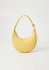 Gul skinnveske med en buet form, glatt tekstur, tynn hank og glidelåslukking. Kjent for sitt minimalistiske design.