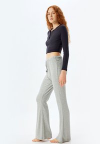 Zwart geribbeld crop top met een knoopsluiting en lange mouwen, gecombineerd met lichtgrijze flare trui broek met een taillestring.