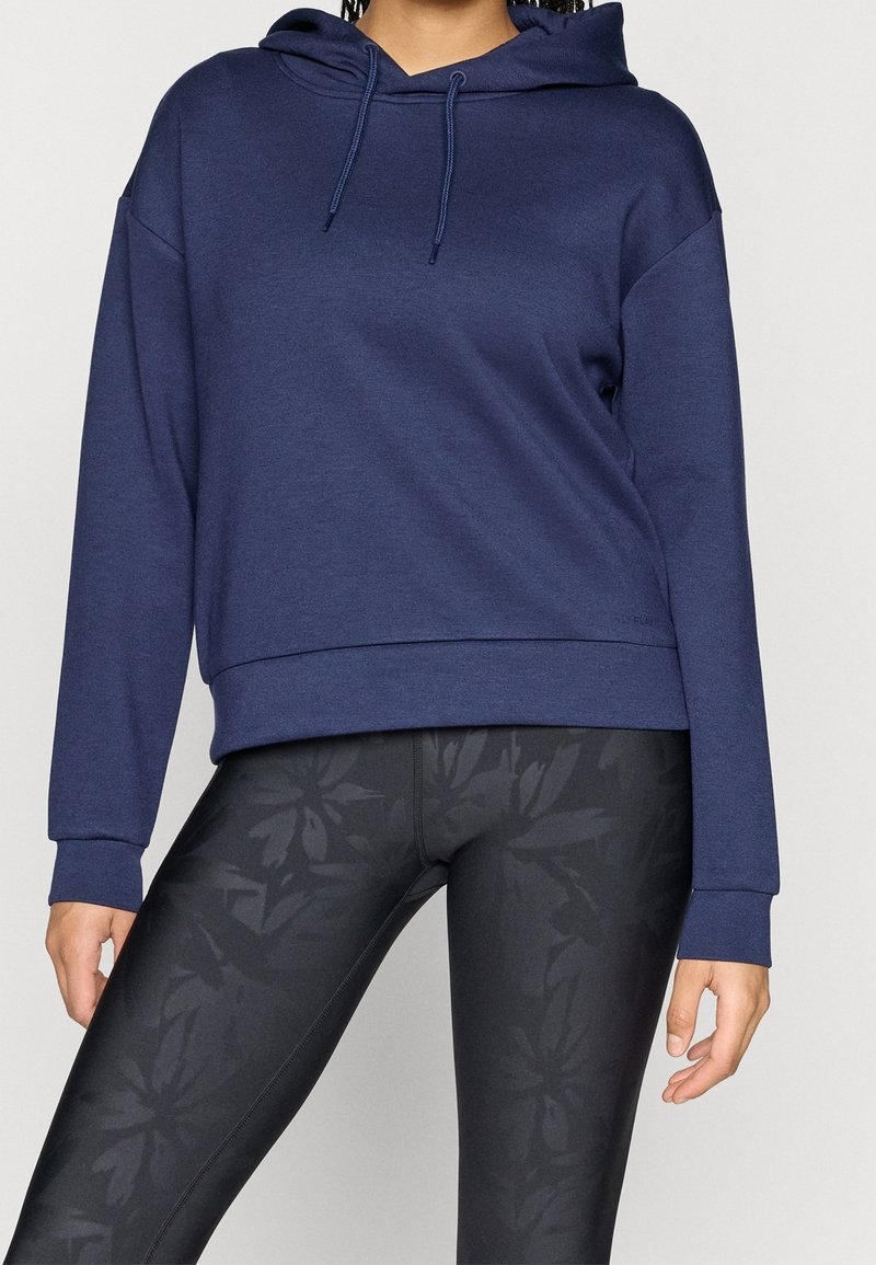 Felpa con cappuccio blu navy con coulisse, vestibilità comoda e polsini a coste. Abbinata a leggings neri con motivo floreale.