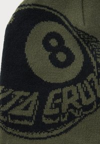 Close-up van gebreide stof met een zwarte achtbal en gedeeltelijke "SCRATCH" tekst in donkergroen en zwarte kleuren.