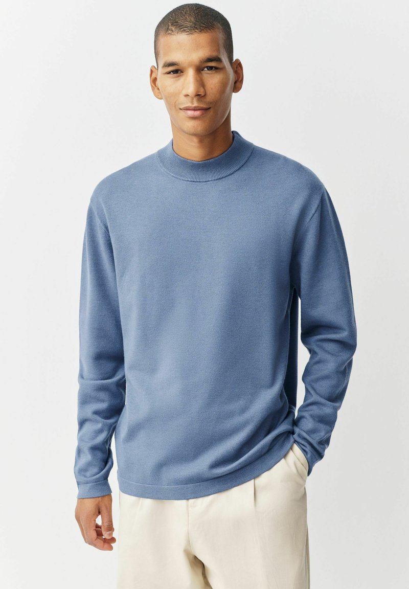 Hellblauer, gestrickter Pullover mit hohem Kragen, langen Ärmeln und lockerer Passform. Der Stoff wirkt weich und hat eine glatte Textur.