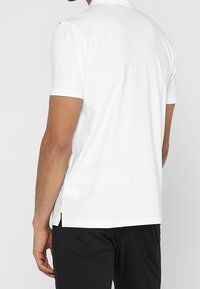 Polo blanc à manches courtes avec une texture lisse, doté de fentes latérales et d'un col classique. La vue de dos montre un minimum de coutures apparentes.
