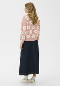 Rózsaszín pulóver fehér virágos applikációkkal, sötét farmer maxi szoknyával párosítva. A modellen bézs sportcipő és fehér zokni van. Hátsó nézet.