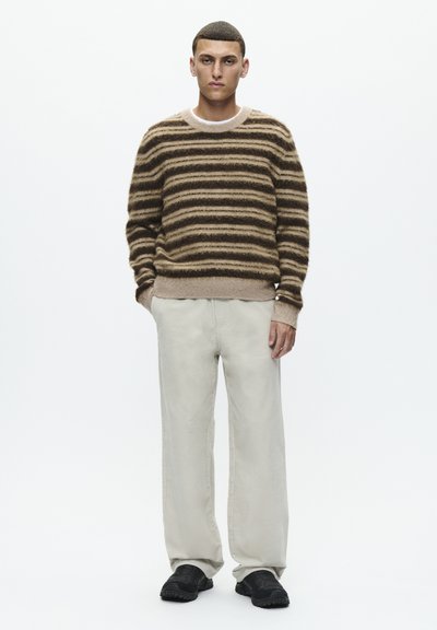 Pull en tricot rayé marron et beige, pantalon beige clair et chaussures noires, avec une coupe décontractée et un matériau texturé.