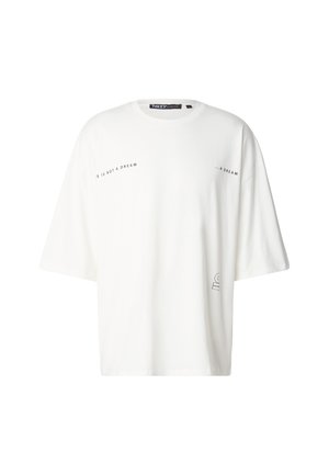 Biała, obszerna bawełniana koszulka z krótkimi rękawami, z czarnym napisem "TO NIE SEN" oraz minimalistyczną grafiką w dolnym prawym rogu.