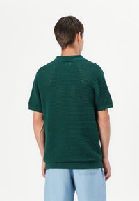 Polo vert à manches courtes avec un motif tissé texturé. Doté d'un col et d'un ourlet côtelés, offrant une coupe décontractée.