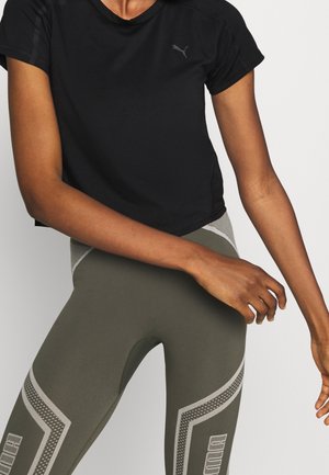 Camiseta atlética negra corta con mangas cortas, con un logo sutil. Combinada con leggins verdes olivo que destacan acentos texturizados.