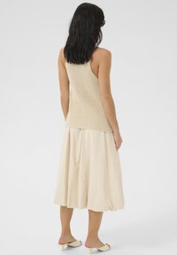 Beige stickad linne, bakvy, tillsammans med en svängig, ljus krämfärgad kjol. Slät textur; avslappnad passform, med enkla sandaler.