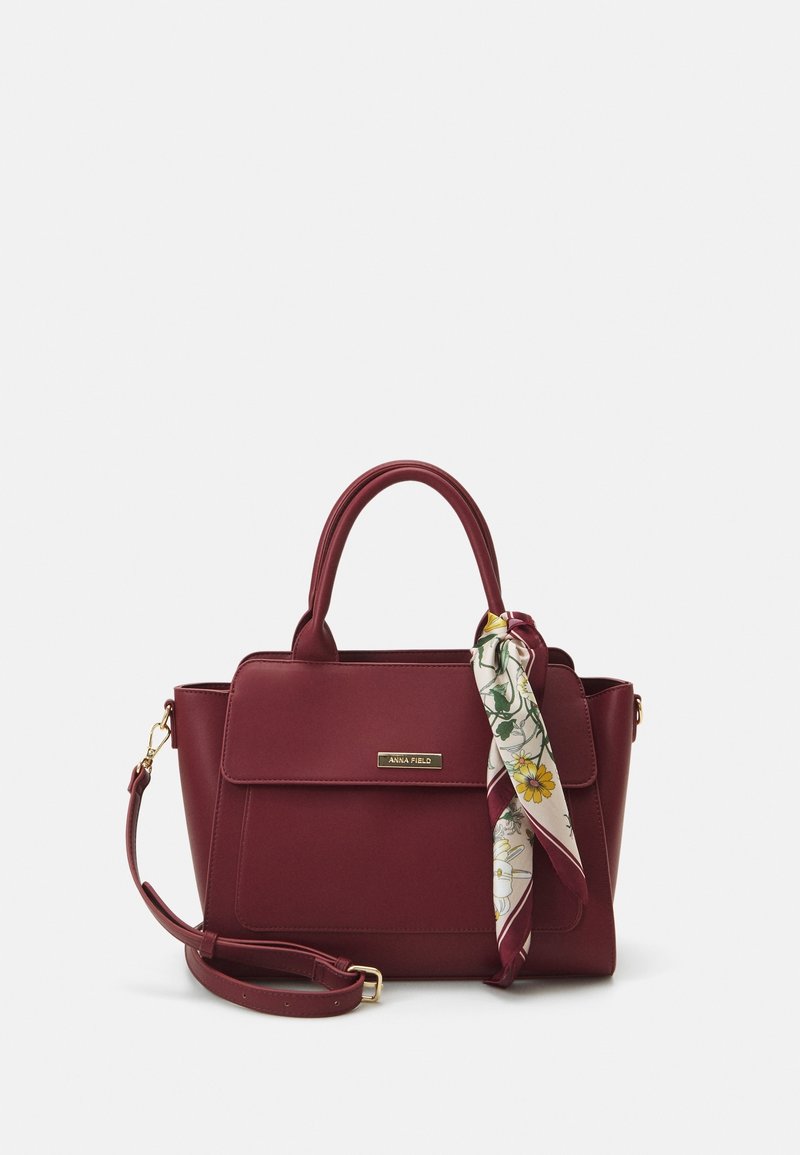 Sac à main bordeaux avec poignées supérieures, bandoulière amovible, poche avant à rabat et foulard à motif floral attaché à une poignée.