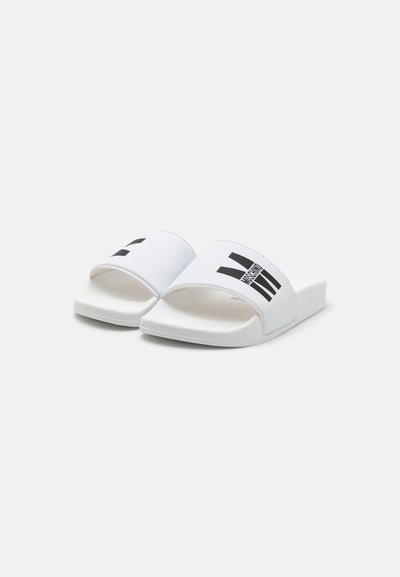 Sandales blanches à glissière avec une large bride ornée d'accents graphiques noirs. Semelle texturée pour une meilleure adhérence. Design à bout ouvert et semelle intérieure rembourrée.