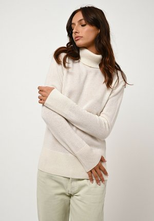 Light cream turtleneck sweater with ribbed cuffs and hem. Soft texture, relaxed fit, and minimalistic design. Paired with light green pants.