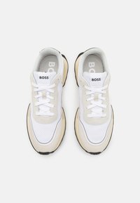 Sneaker sportive bianche e beige realizzate in materiali mesh e suede, punta rotonda, chiusura con lacci, suola nera spessa e linguetta con marchio.