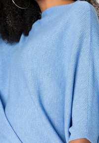 Hellblaues Strickoberteil mit lockerer Silhouette, kurzen Ärmeln und strukturiertem Rippenmuster. Der Stoff wirkt weich und leicht.