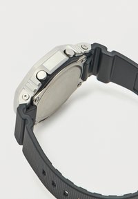 Ασημένιου τόνου κάσα ρολογιού με υφασμένο μαύρο λαστιχένιο λουράκι. Διαθέτει δύο πλευρικά κουμπιά και ομαλή μεταλλική πίσω όψη. Εξαγωνικό σχήμα.