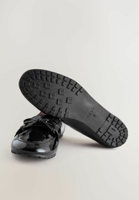 Svarta lackläders loafers med rund tå, dekorativ rosett och strukturerad gummisula med ett mönstrat mönster.