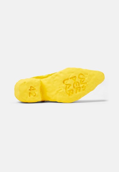 Helle gelbe Schuhsohle mit strukturiertem, unebenen Oberfläche. Verfügt über eine eingeprägte Größe "42" und ein stilisiertes Logo. Das markante Design verbessert den Halt.
