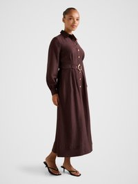 Brown, long-sleeve belted dress with a button-down front, featuring a circular gold buckle detail and a relaxed fit to the ankle.