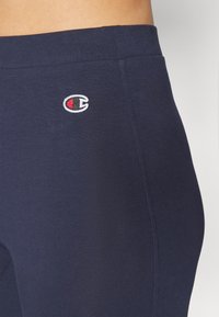 Leggings blu navy realizzati in un tessuto di cotone elasticizzato. Presentano un logo ricamato in alto a sinistra. Texture liscia e design aderente.
