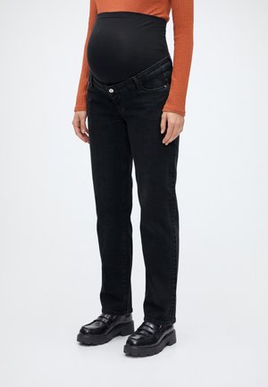 Persona embarazada que lleva vaqueros premamá negros con cintura elástica, combinados con zapatos negros robustos y una camiseta de manga larga naranja.