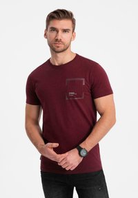 Burgundyröd bomulls t-shirt med rund hals, korta ärmar och en genomskinlig fickdetalj med text. Parat med svarta slitna jeans.