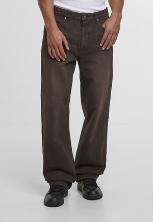 Barna színű, laza szabású farmernadrág, gombos lezárással, első zsebekkel és texturált felülettel. Fekete tornacipővel viselve.