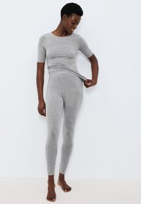 Šedý přiléhavý top s krátkými rukávy, doplněný o šedé legíny ve stejném odstínu. Hladká textura, minimalistický design, elastický materiál. Bez vzorů nebo akcentů.