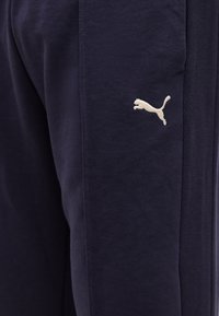 Κοντινή λήψη μπλε σκούρου παντελονιού από ύφασμα με μικρό λευκό λογότυπο πούμα που πηδά κεντημένο στο πλάι.