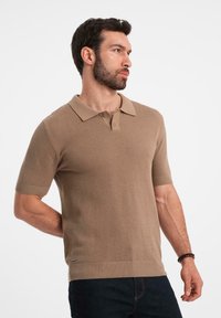 Kortärmad polo i beige, texturerat stickat tyg, med en klassisk krage, tre knappar och ribbad nederkant och ärmslut.