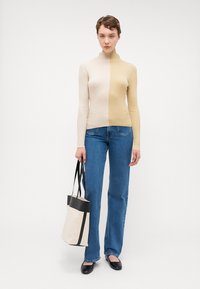 Pulover cu guler înalt, cu caneluri, în două nuanțe, bej și maro deschis. Asortat cu blugi din denim albastru și o geantă crem cu accente negre.
