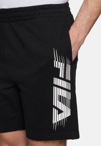 Svarta shorts med resår i midjan. Har en framträdande vit grafisk design på vänster sida. Mjukt bomullsmaterial, avslappnad passform.