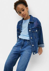 Džínová bunda so detailmi hviezd, svetlomodré tričko a rifle s vysokým pásom, všetko v rôznych odtieňoch modrej, s prepracovanými akcentmi na šití.