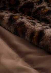 Tissu en fausse fourrure à imprimé léopard avec une texture douce et moelleuse, superposé sur un tissu satin brun lisse. Le contraste des textures est marqué.