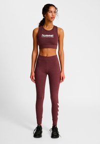 Vinröd sportcrop top med vit logotyp och matchande högmidjade leggings med vita accentremsor på sidorna. Svarta sneakers.