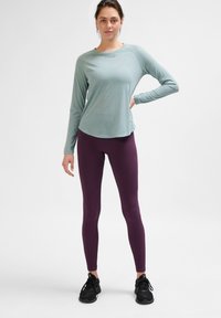 Helles Türkis langärmliges Oberteil mit Rundhalsausschnitt, kombiniert mit gerippten dunkellila Leggings und schwarzen Sportschuhen. Einfaches, minimalistisches Design.